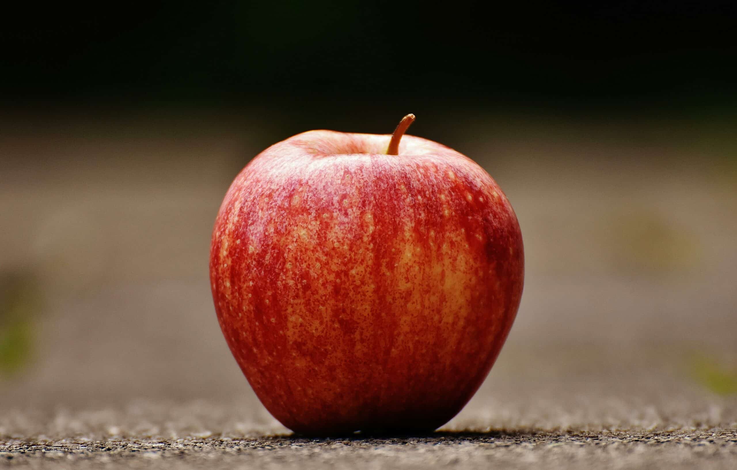A vibrant red apple resting on a textured outdoor surface, showcasing natural beauty and freshness.