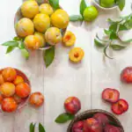 Top view of vibrant fresh plums and limes with green leaves on a wooden table.