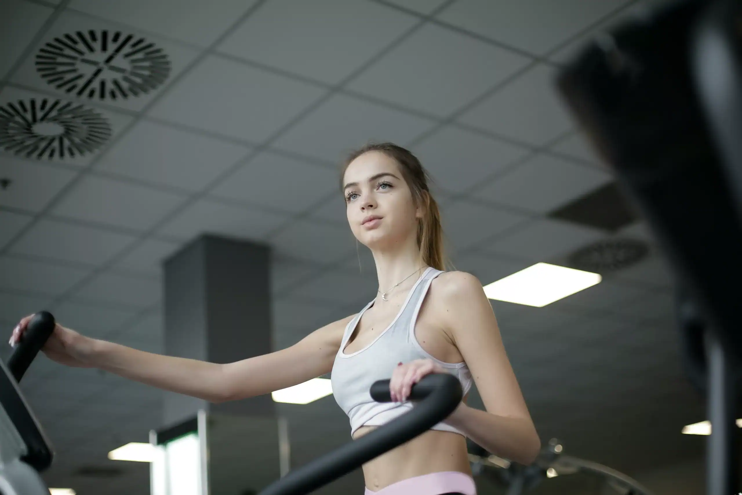 Focused young woman on elliptical trainer in gym, demonstrating fitness and determination.