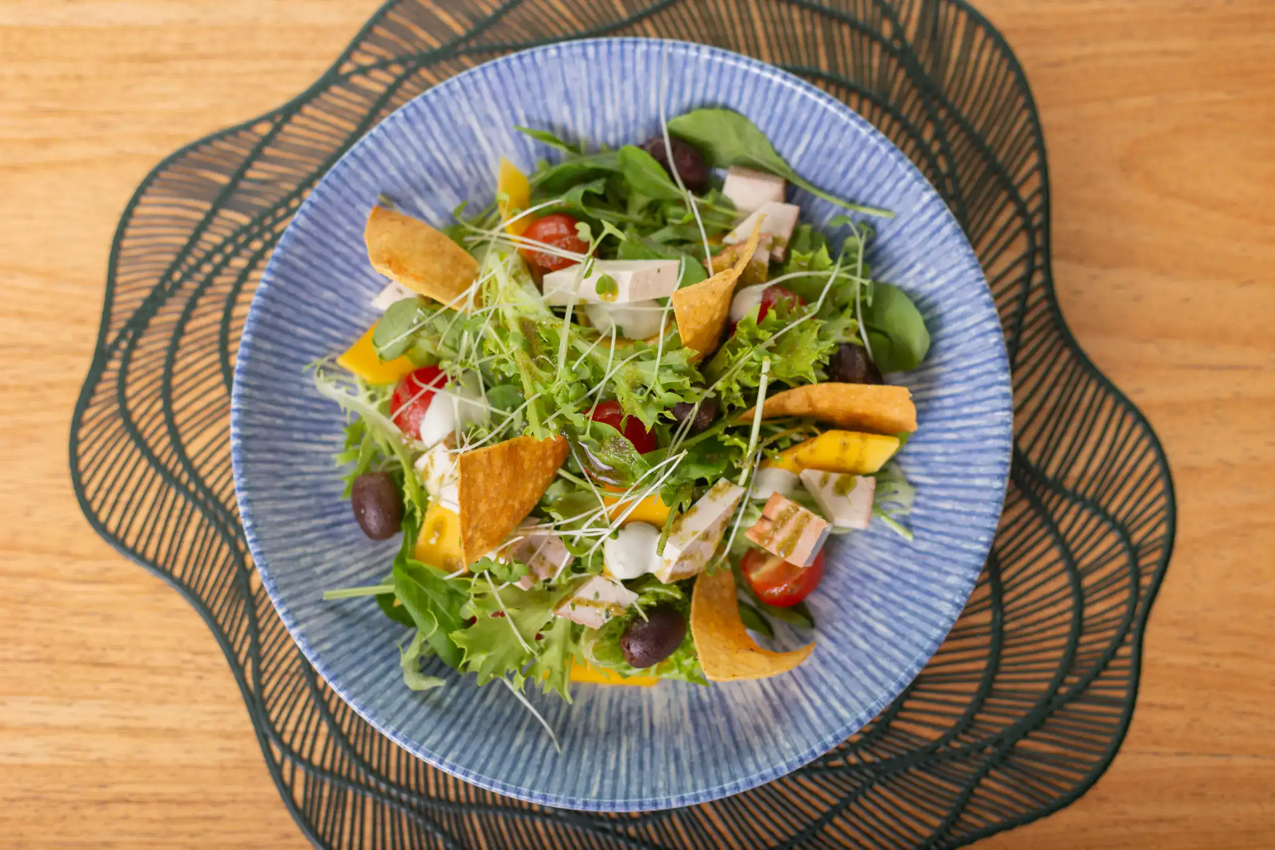 A vibrant Mediterranean salad featuring mixed greens, tomatoes, olives, and tortilla chips in a blue bowl.