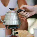 A close-up of an outdoor coffee setup with a metal kettle on a portable stove, emphasizing lifestyle and travel.