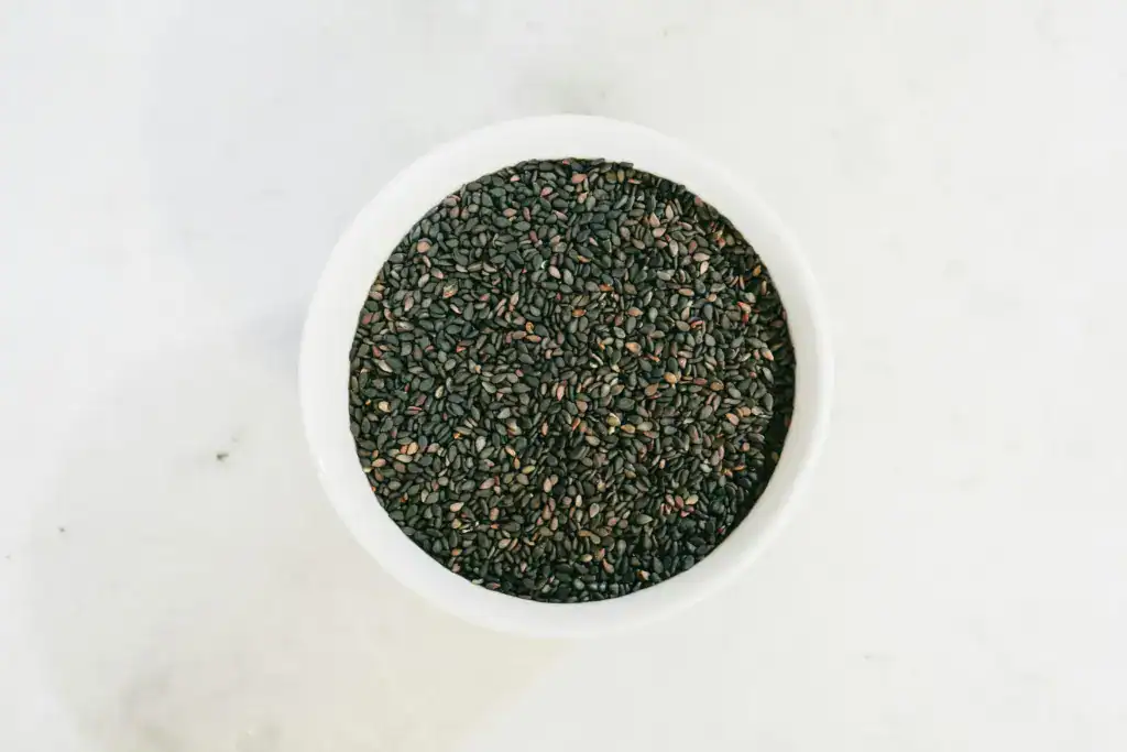 High-angle view of black sesame seeds in a white bowl on a marble surface, perfect for food photography.