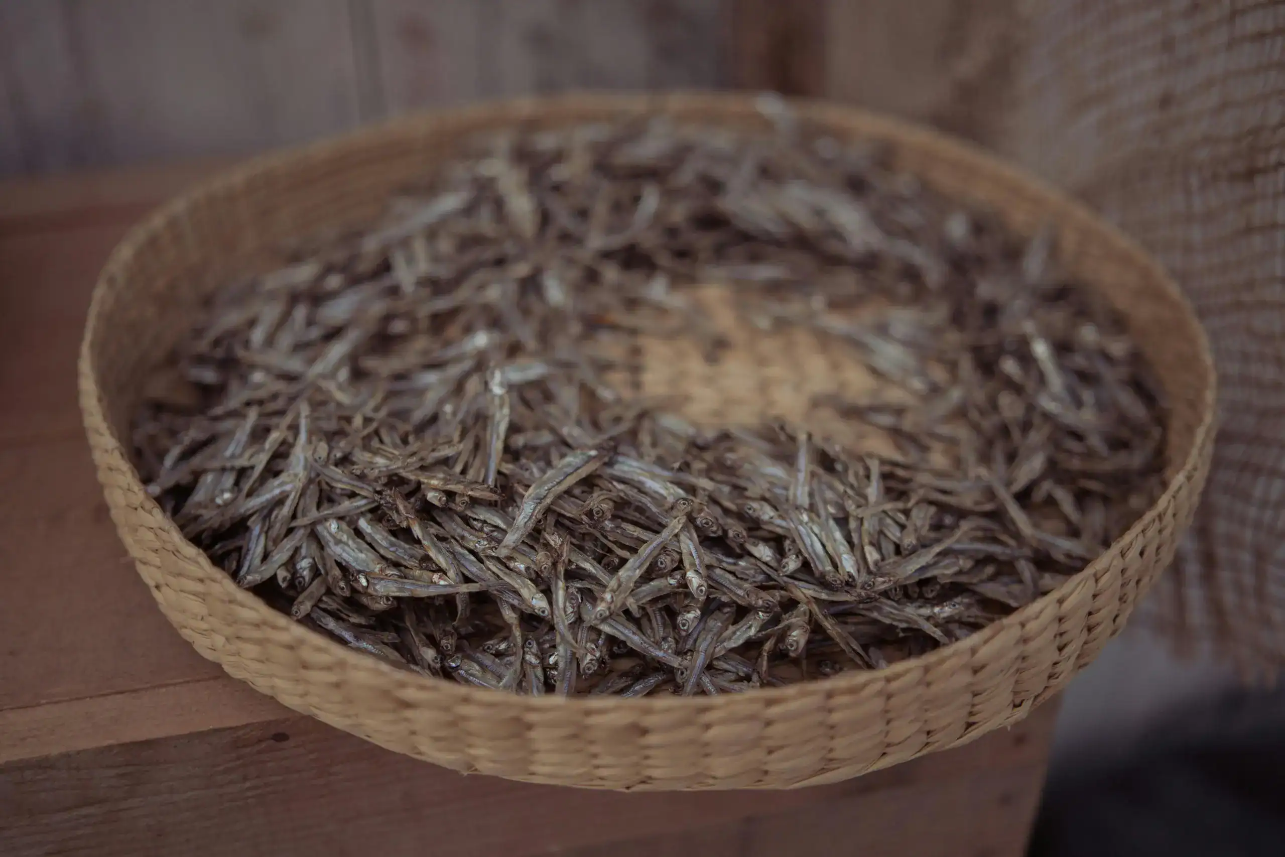 A woven basket filled with dried fish placed outdoors, showcasing traditional drying methods.