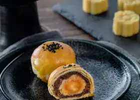 Mouthwatering Chinese egg yolk pastry with a rich filling on a dark plate, perfect for festive celebrations.