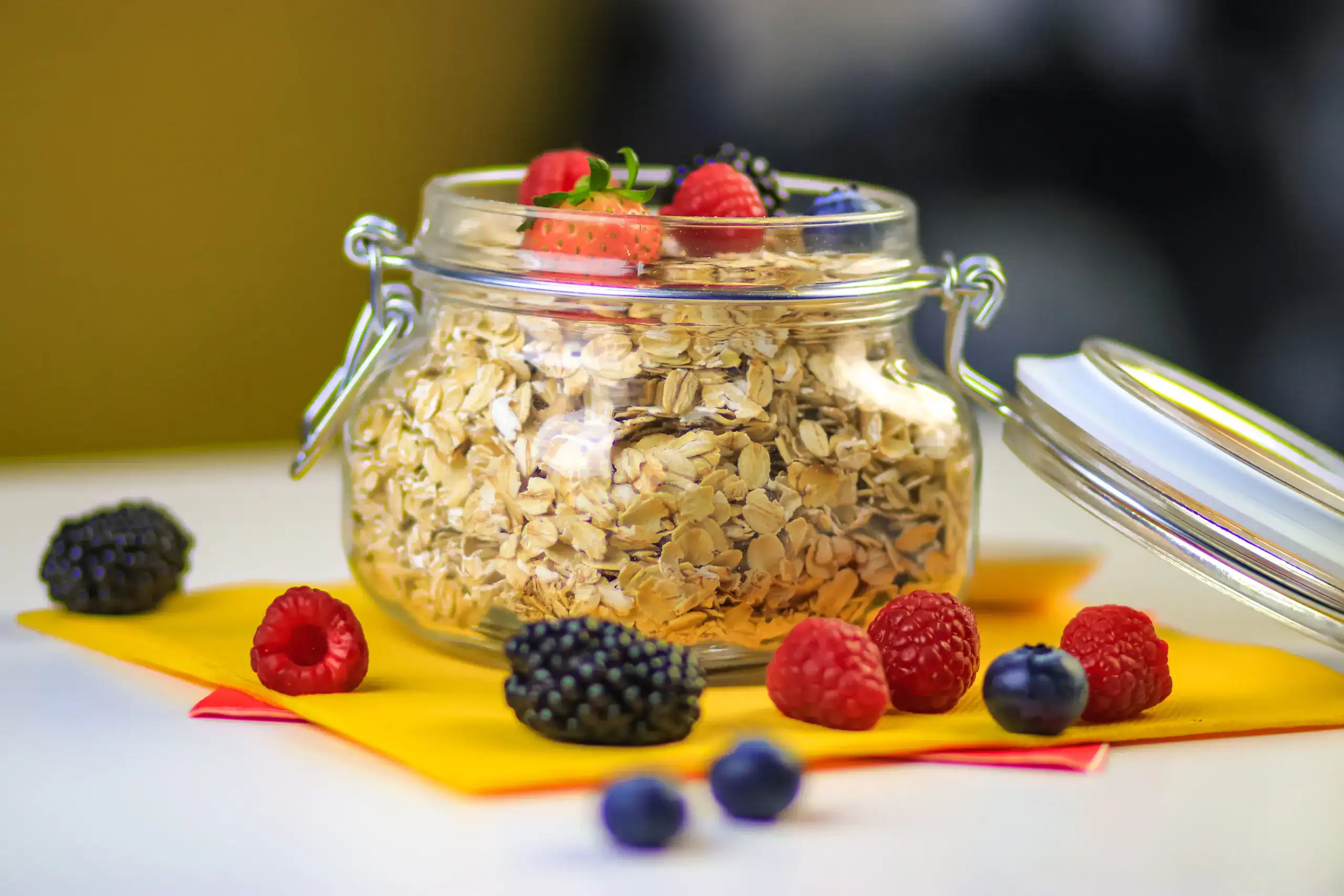 Glass jar of oats surrounded by fresh berries on a colorful background.