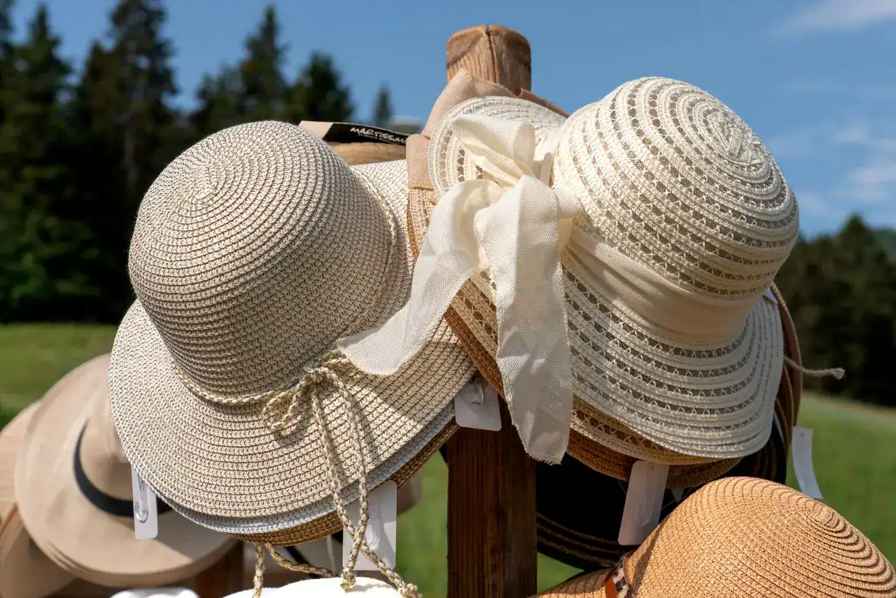 Close-up of stylish sun hats on wooden stand against sunny outdoor backdrop.